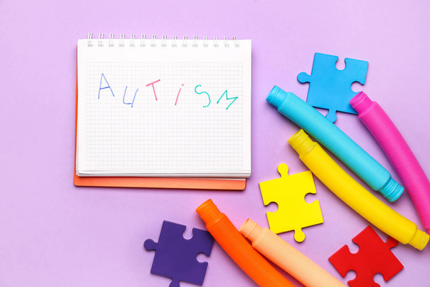 Quaderno con parola AUTISMO, pezzi puzzle e Pop Tubes su sfondo lilla - Foto, immagini