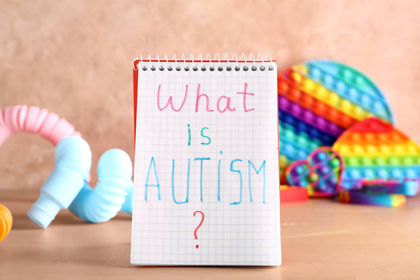 Notebook with text WHAT IS AUTISM? and toys on color background - Foto, afbeelding