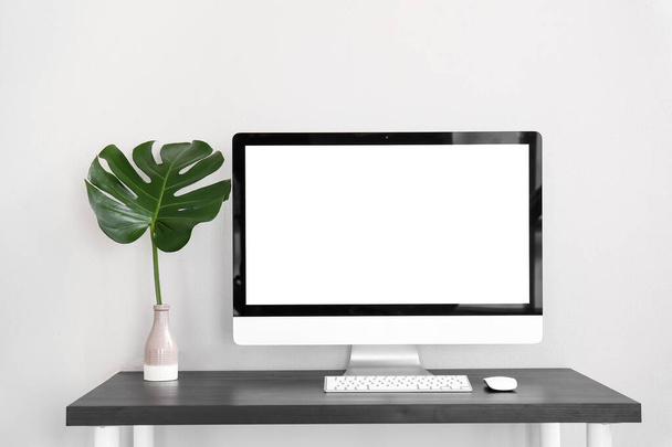 Workplace with computer and palm leaf in vase near light wall - Photo, Image