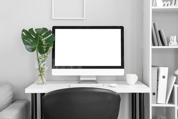 Pracoviště s počítačem, rostlinné větve ve ve váze a pohár u světelné stěny - Fotografie, Obrázek