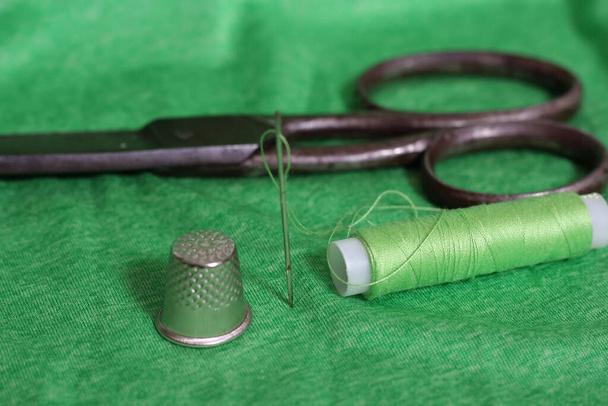 Cívka zelené nitě, náprstek a jehla na zelené tkanině zblízka - Fotografie, Obrázek