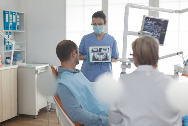 Enfermera especialista en ortodoncia que usa mascarilla facial que muestra radiografía dental - Foto, Imagen
