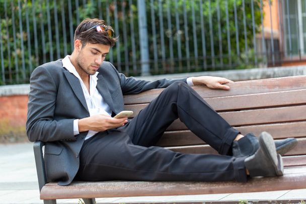 beautiful elegant dark-haired Italian boy with jacket and trousers sitting on the bench. High quality photo - Photo, Image