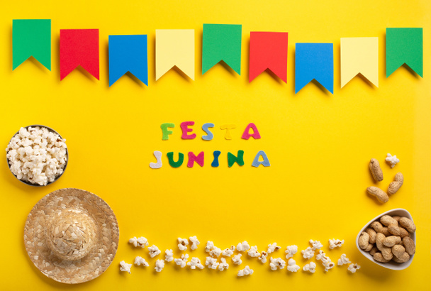 Концепция летнего фестиваля Carnival Brazilian Festa Junina. Бразильская соломенная шляпа, попкорн, арахис и красочные флаги на желтом фоне, вид сверху. Дизайн для поздравительной открытки, приглашения или праздничного плаката - Фото, изображение