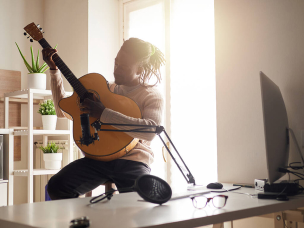 Young man is singing and playing guitar while making an audio recording at home - Foto, immagini