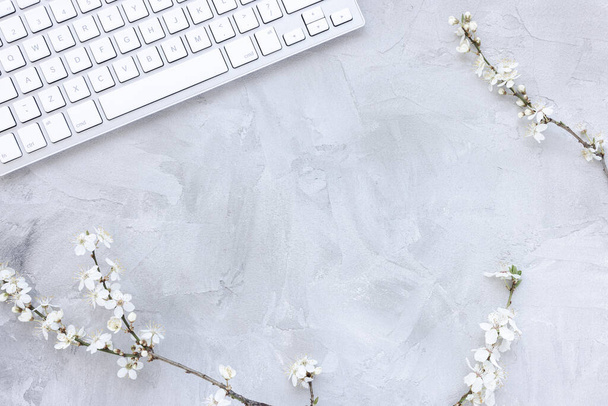 Computer keyboard on spring gray background with white cherry blossom flowers, copy space - Photo, Image