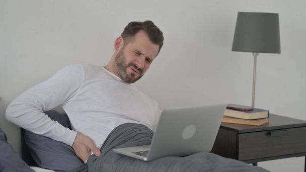 Muž s bolestí zad pracující na notebooku v posteli - Fotografie, Obrázek