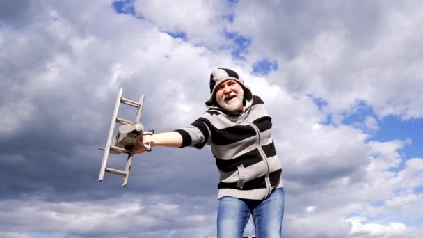 Happy greybeard man stel je voor vliegen op houten vliegtuig in de lucht, doen alsof vliegen - Video