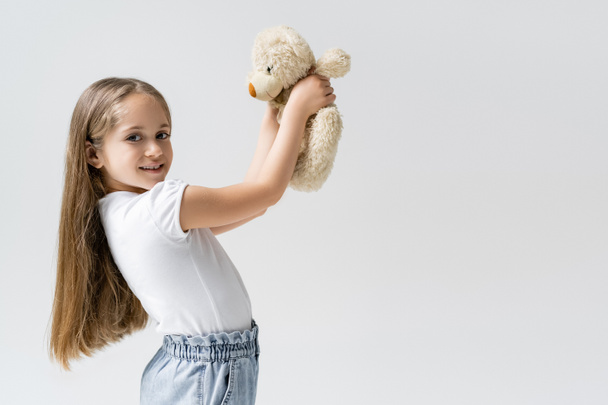 happy girl with teddy bear smiling at camera isolated on grey - Photo, Image