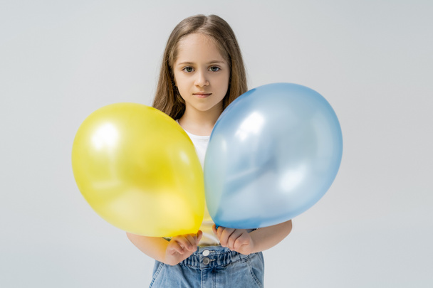 Ukraińska dziewczyna trzyma niebiesko-żółte balony patrząc na aparat odizolowany na szarości - Zdjęcie, obraz
