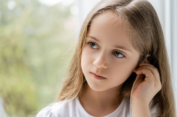menina com cabelo longo ajustando fone de ouvido perto da janela embaçada - Foto, Imagem