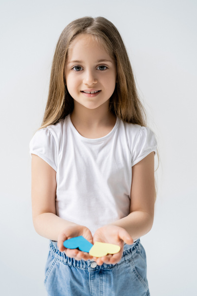 улыбающаяся девушка с длинными волосами и голубыми и желтыми бумажными сердцами, изолированными на сером - Фото, изображение