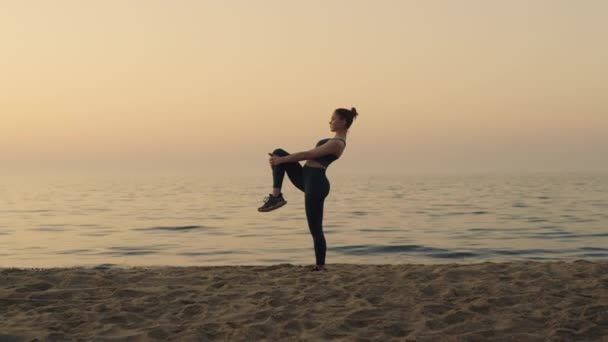 Sportovní dívka drží kolena natahující nohy na pláži. Sportovní žena zahřívá nohy. - Záběry, video