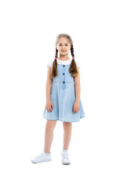 pełny widok długość dziewczyna w niebieski pasek sukienka uśmiecha się do kamery podczas stojąc na białym - Zdjęcie, obraz