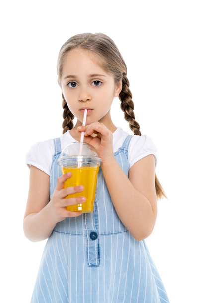 menina em azul vestido cinta beber suco de laranja e olhando para a câmera isolada no branco - Foto, Imagem