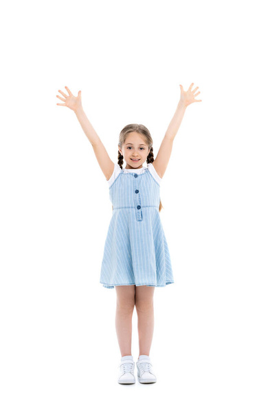 plná délka pohled na dívku v modrém řemínku šaty stojící se zvednutýma rukama na bílém - Fotografie, Obrázek