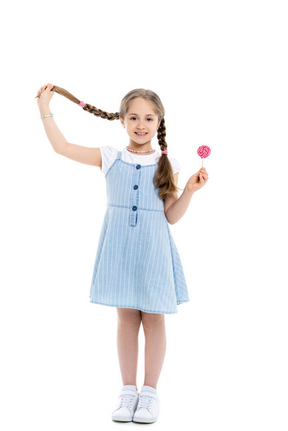 full length view of cheerful girl holding braid and lollipop on white - Foto, imagen