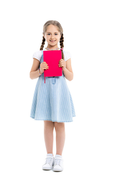 full length view of happy girl holding bright pink copy book on white - Foto, Imagen