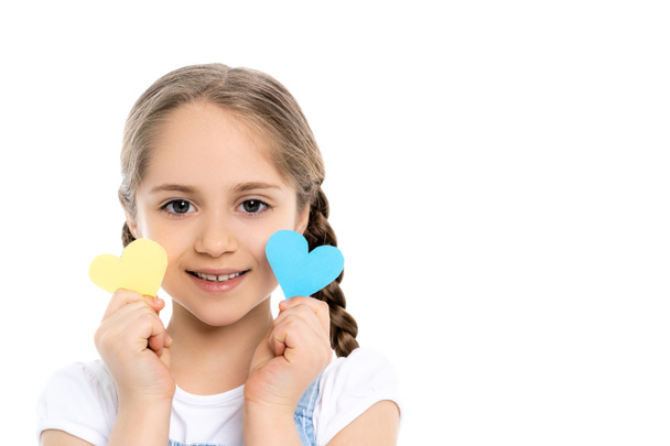 glimlachend Oekraïens meisje met papieren harten met blauwe en gele nationale kleuren geïsoleerd op wit - Foto, afbeelding