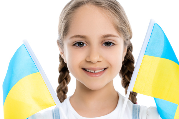 portrait of smiling patriotic girl near ukrainian flags isolated on white - Photo, Image