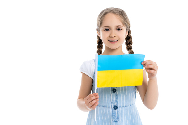 lachend meisje met kleine Oekraïense vlag kijkend naar camera geïsoleerd op wit - Foto, afbeelding