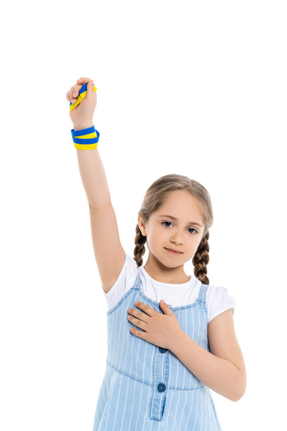 Mavi ve sarı kurdeleli vatansever Ukraynalı kız elini kaldırmış beyazların üzerinde dururken kalbe dokunuyor. - Fotoğraf, Görsel