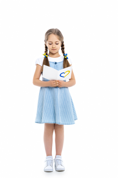 full length view of girl reading postcard with blue and yellow heart on white - Fotó, kép
