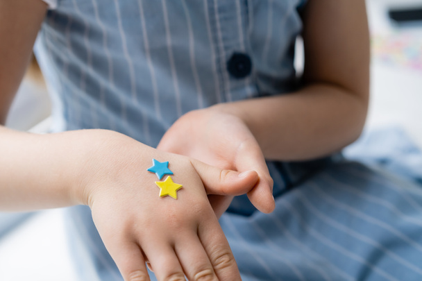 Ausgeschnittene Ansicht eines Kindes mit blauen und gelben Sternen auf der Hand - Foto, Bild