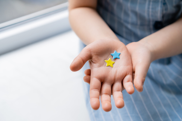 vue partielle de l'enfant avec des étoiles bleues et jaunes sur la paume ouverte - Photo, image