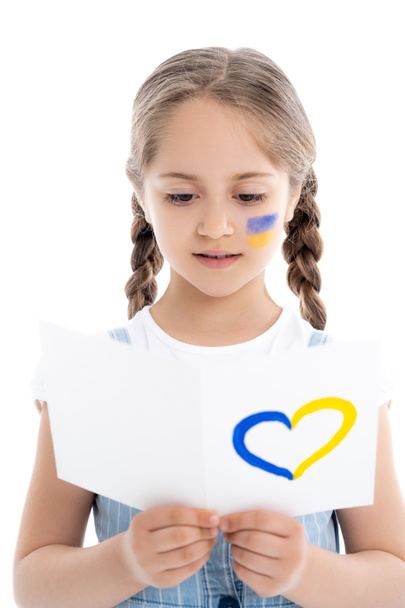 girl with ukrainian flag on face reading card with blue and yellow heart isolated on white - Photo, Image