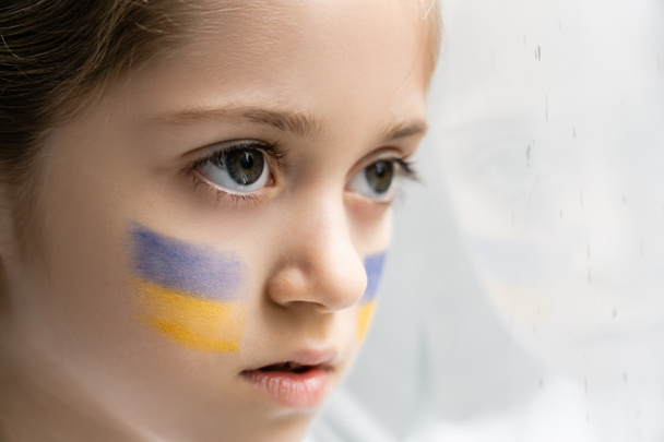 close up portrait of ukrainian child with national flags on face on white background - Photo, Image
