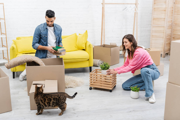 Positive interracial couple unpacking packages near bengal cat at home  - Photo, Image