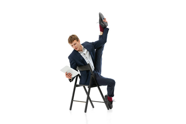 Portrait of young handsome man, office worker sitting on office chair and using tablet isolated over white background - Foto, afbeelding