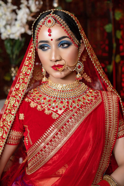 Portrait of a beautiful bride in elegant wedding dress with bridal jewelry & makeup with gorgeous lehenga, studio indoor with heavy bokeh lighting. Sensuality and glamour. Portrait of beautiful adult bride in traditional non bengali dress & Jewelry. - Photo, Image