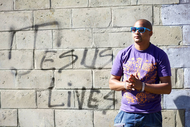 Πνευματικό κλοπιμαία. Πυροβολισμός ενός νεαρού άνδρα που στεκόταν μπροστά από έναν τοίχο με γκράφιτι πάνω του.. - Φωτογραφία, εικόνα