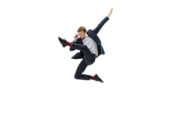 Hombre joven en ropa de oficina saltando con teléfono retro aislado en fondo blanco estudio. Negocios, start-up, open-space, concepto de inspiración. - Foto, imagen