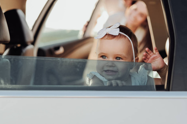 Toddler Caucasian Girl Sitting Inside the Car and Waving Hand Imitating Hello Through the Window - Foto, Imagem