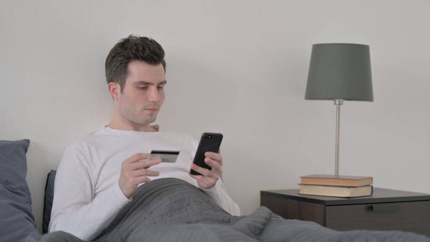 Man Making Online Payment on Smartphone in Bed - Foto, afbeelding