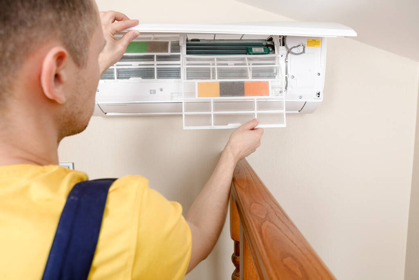 Male technician cleaning air conditioner indoors - Foto, imagen