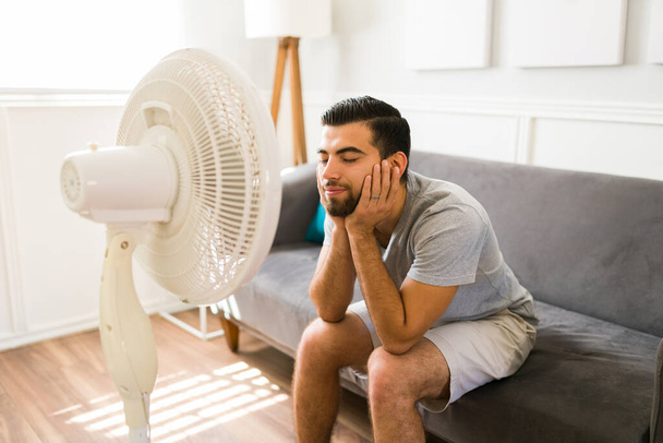 Happy young woman feeling better at home while relaxing in front of the electric fan during a bad heat wave - Foto, Imagen
