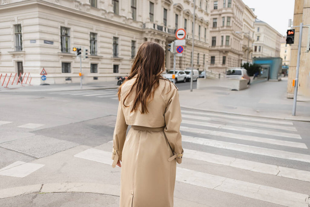 back view of woman in trench coat walking on street of european city  - Foto, imagen