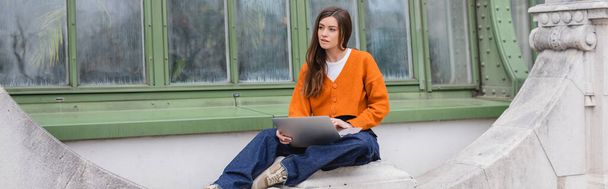 young woman in jeans and orange cardigan using laptop on rooftop of building, banner - Foto, immagini