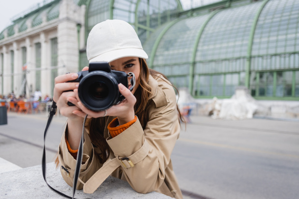 young photographer in trench coat and baseball cap taking photo on digital camera  - Photo, Image