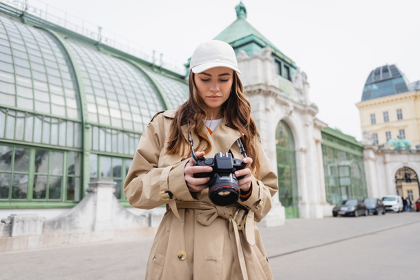 photographer in trench coat and baseball cap holding digital camera in european city - Фото, зображення
