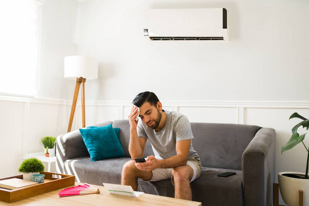 Αναστατωμένος άνθρωπος εφίδρωση κατά τη διάρκεια ενός κύματος καύσωνα το καλοκαίρι, ενώ στο σπίτι με ένα κρύο ac μονάδα - Φωτογραφία, εικόνα