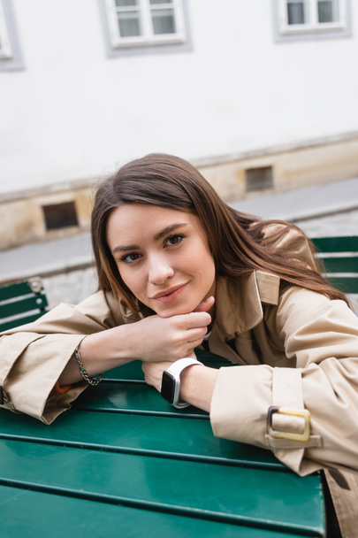 bonita jovem mulher na moda casaco de trincheira inclinado na mesa de café no terraço de verão  - Foto, Imagem