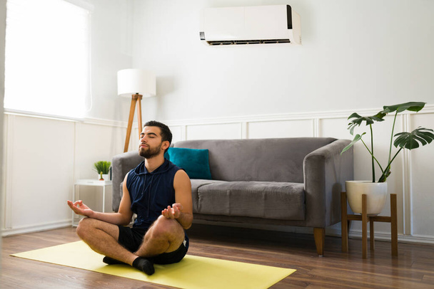 Расслабленный фитнес-человек, делающий посредничество и расслабление с холодным кондиционером  - Фото, изображение