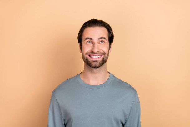 Photo of young cheerful man curious interested look empty space thoughtful minded isolated over beige color background - Foto, imagen