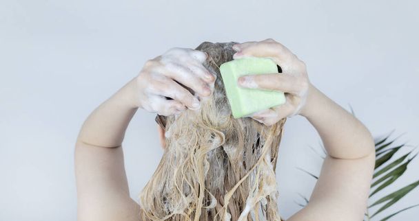 Solid hair shampoo. Close-up of a blonde girl in the bathroom, which lathers her hair with dry shampoo. Lots of foam and peek effect. - Foto, imagen