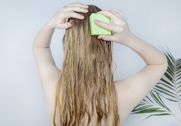 Shampooing pour cheveux solides. Gros plan d'une fille blonde dans la salle de bain, qui se fait mousser les cheveux avec un shampooing sec. Beaucoup de mousse et d'effet de coup d'oeil. - Photo, image